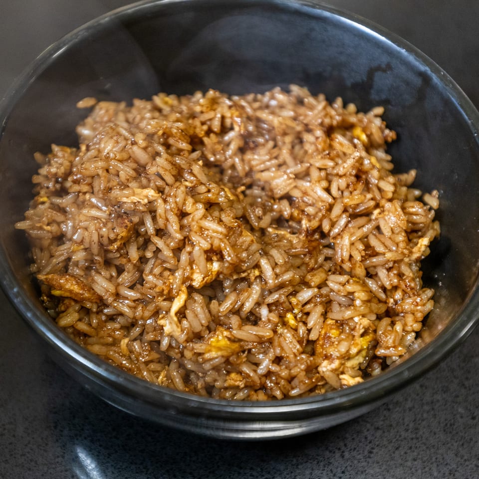 Steaming hot Thai fried rice with egg in a black bowl, ready to be served.