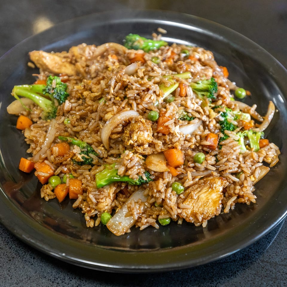 Thai Esane's chicken fried rice with broccoli, carrots, peas, and onions on a black plate.