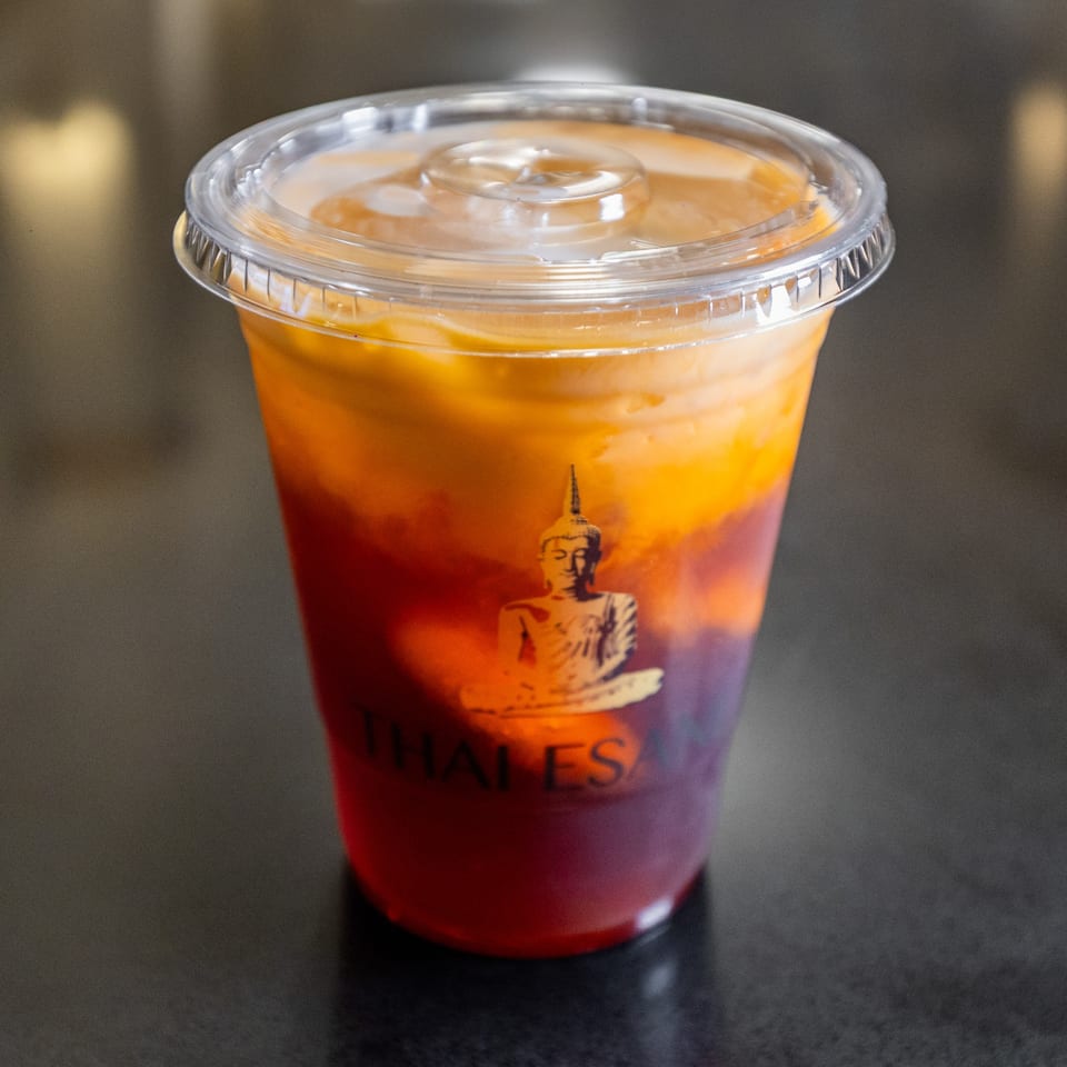 Thai Esane's vibrant Thai iced tea in a clear cup with a Buddha logo.