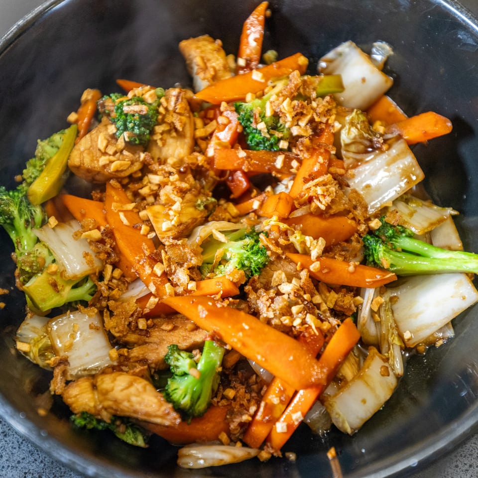 Thai stir-fry with chicken, broccoli, carrots, and bok choy, topped with crispy garlic.