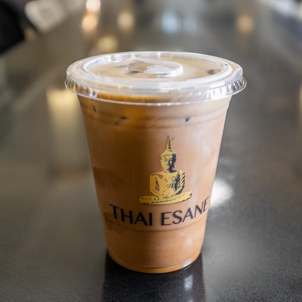 Iced Thai tea in a clear plastic cup with the Thai Esane logo on a dark table.