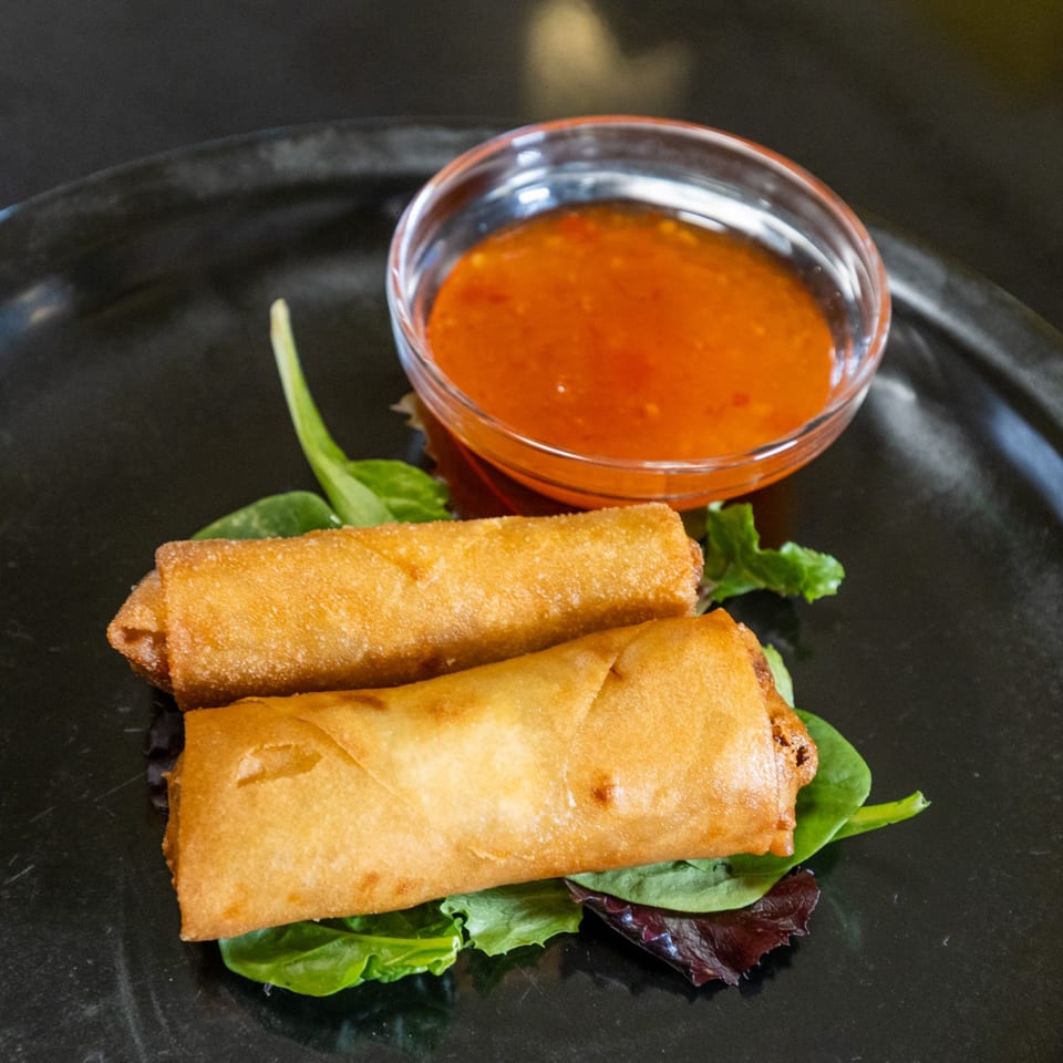 Two crispy Thai Esane spring rolls on lettuce with a side of sweet chili sauce.